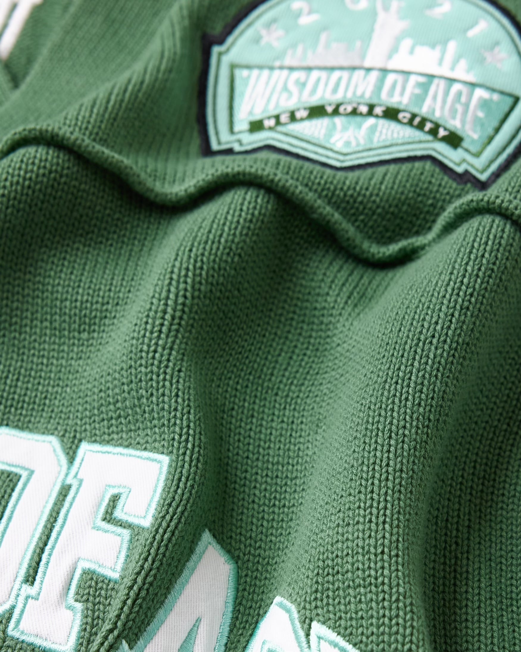 Close-up of a sage green football jersey with 'Wisdom of Age' branding