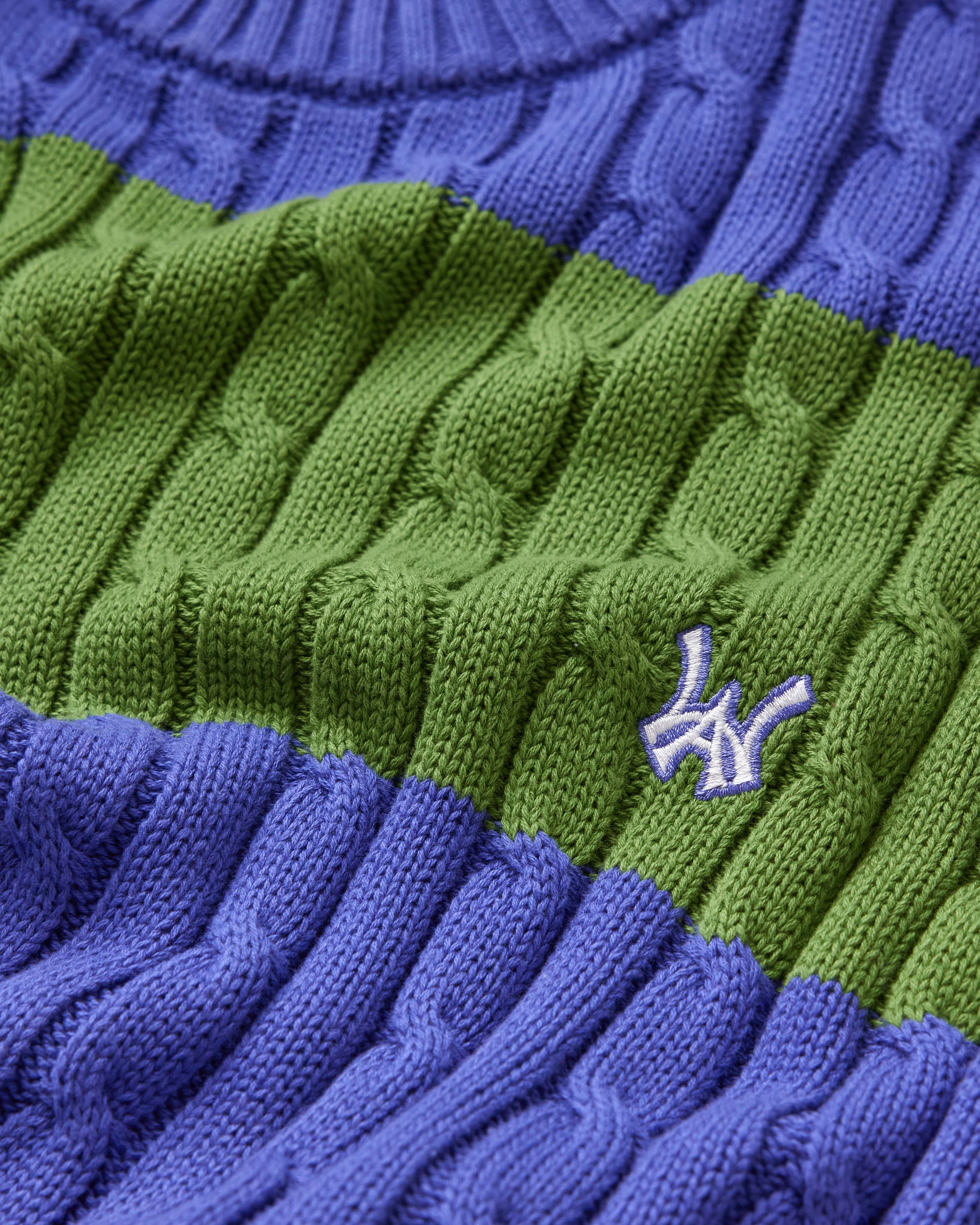 Close-up of a green and blue cable knit sweater with the WA logo