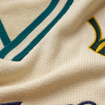 Close-up of a cream knitted jersey with green and yellow text and design elements.
