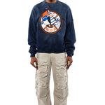 Male Model wearing a navy sweatshirt with a logo and beige cargo pants on a white background