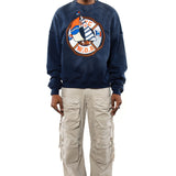 Male Model wearing a navy sweatshirt with a logo and beige cargo pants on a white background