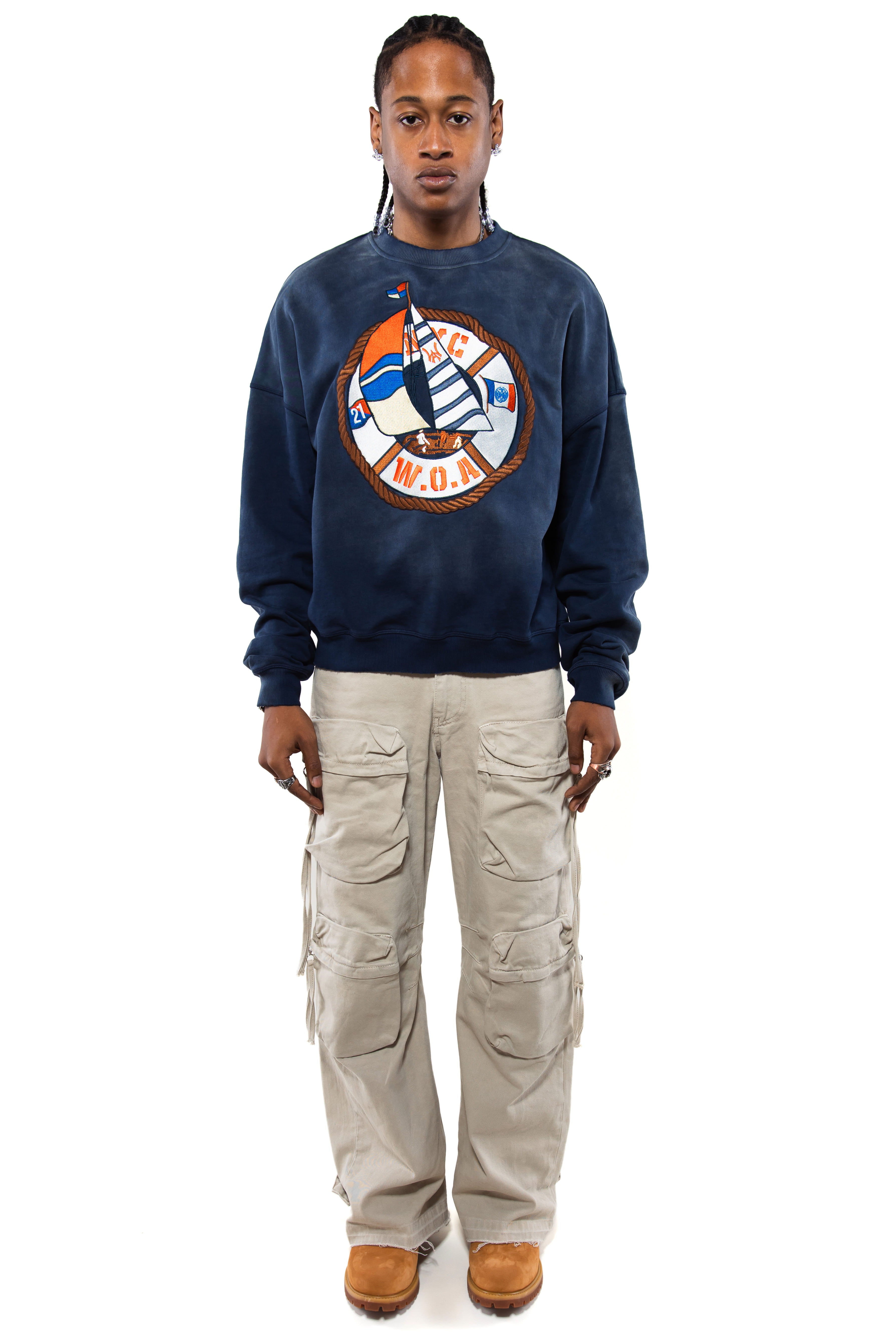 Male Model wearing a navy sweatshirt with a logo and beige cargo pants on a white background