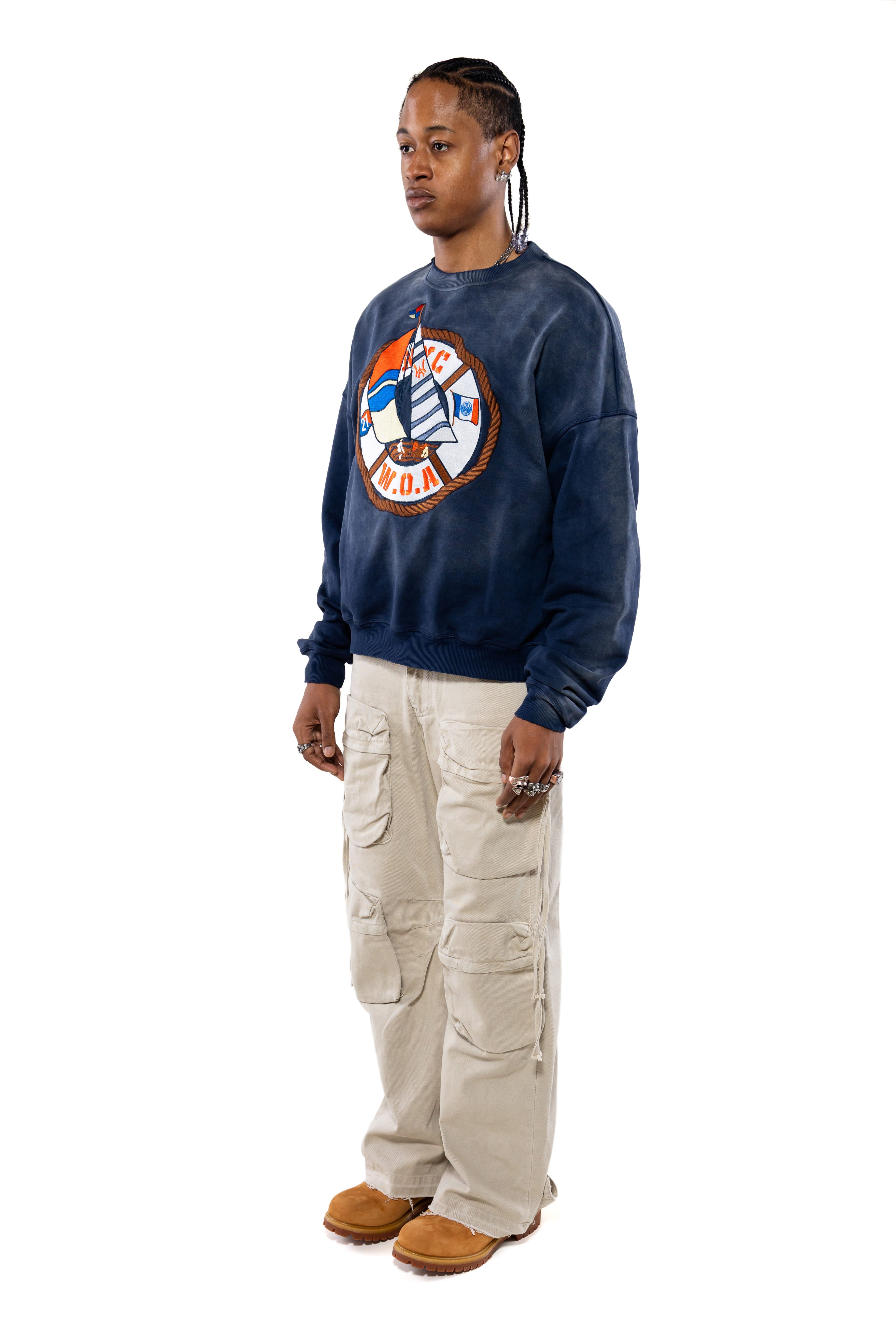 Side view of a Male Model wearing a navy sweatshirt with a logo and beige cargo pants on a white background