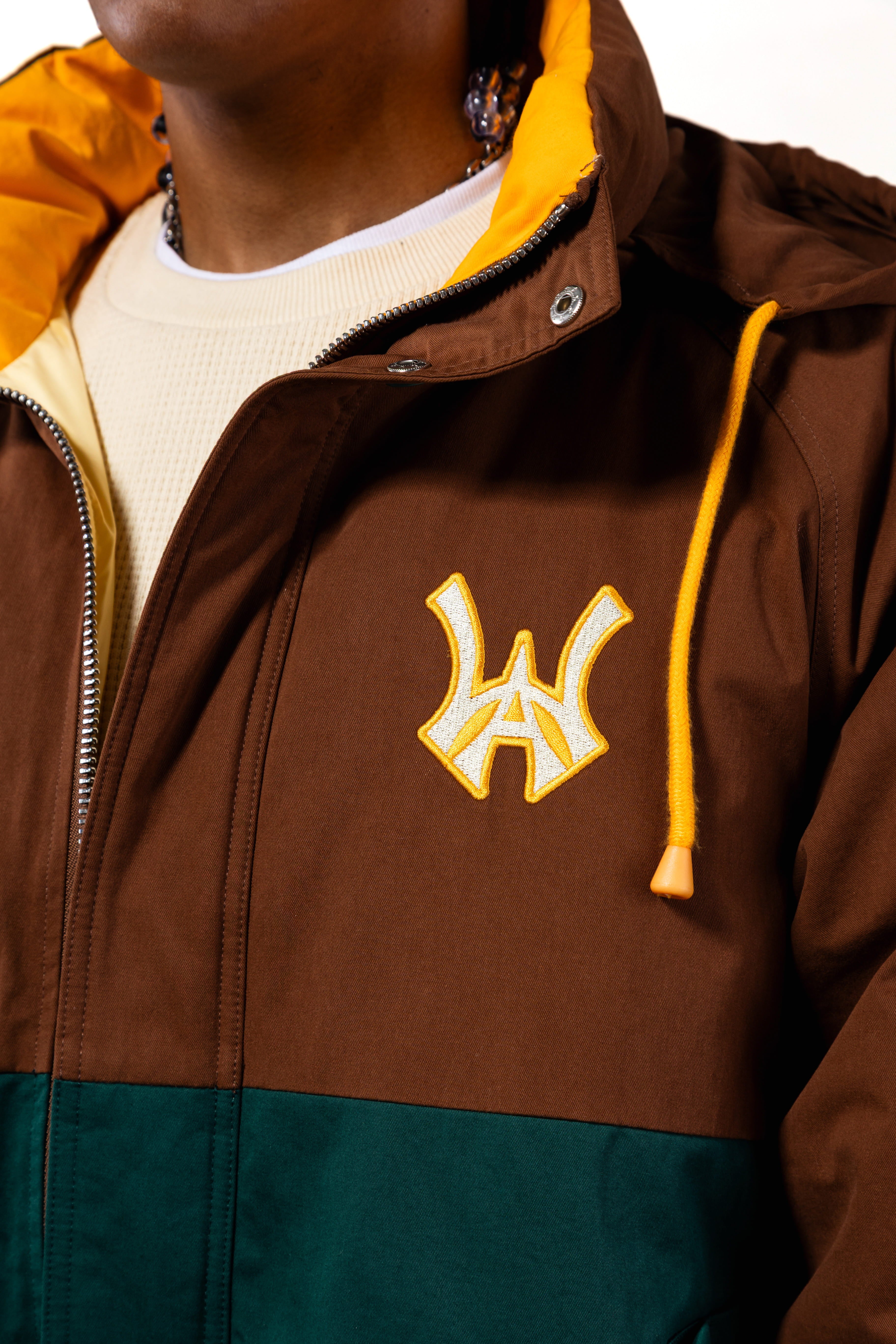 Close up of Brown jacket with yellow hood and embroidered 'WA' logo with a yellow outline on a white background