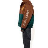 Side view of a Male Model wearing a brown and forest green jacket with yellow accents on a white background. 'Wisdom Of Age' written on the sleeve.