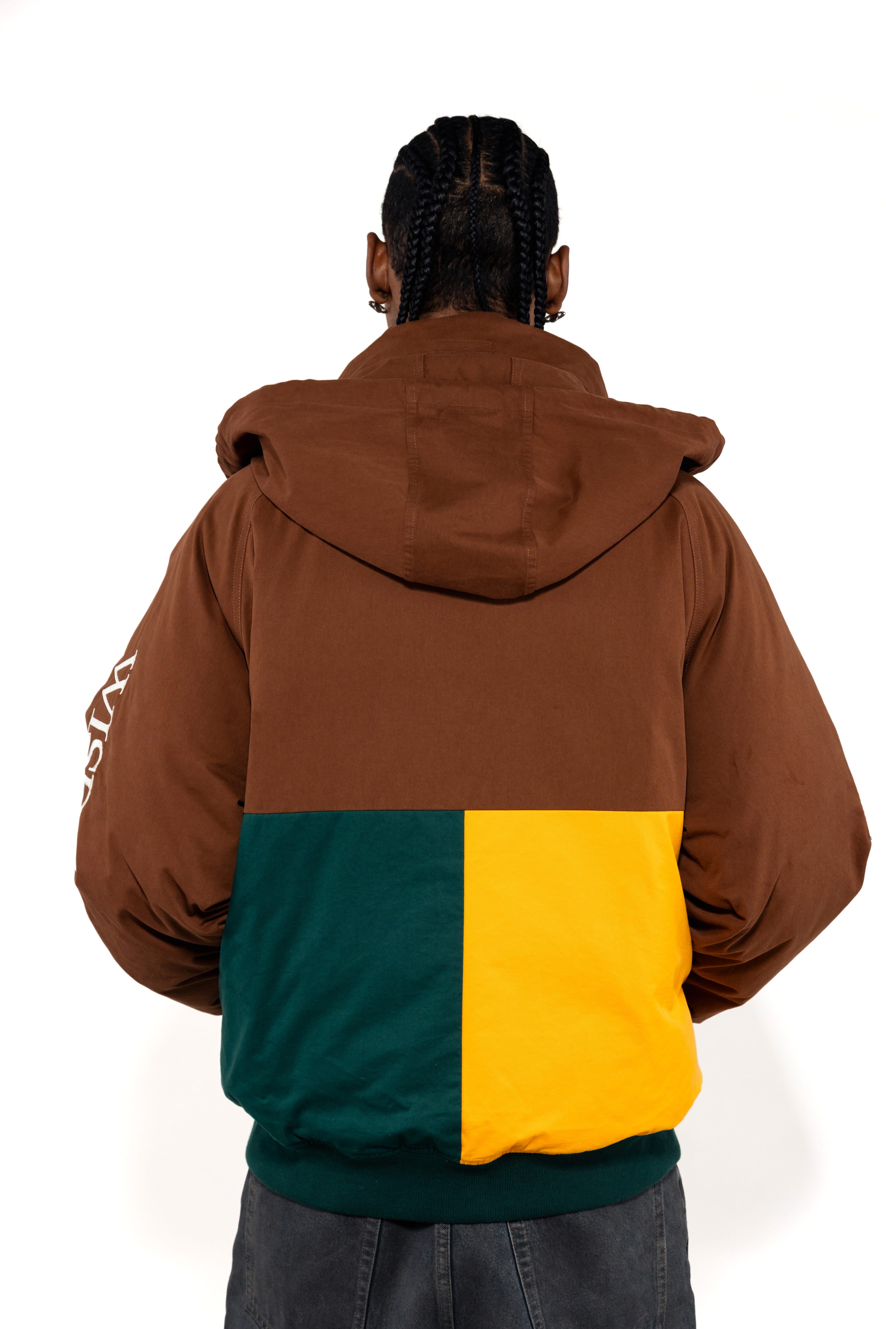 Rear view of a Male Model wearing a brown and forest green jacket with yellow accents on a white background.