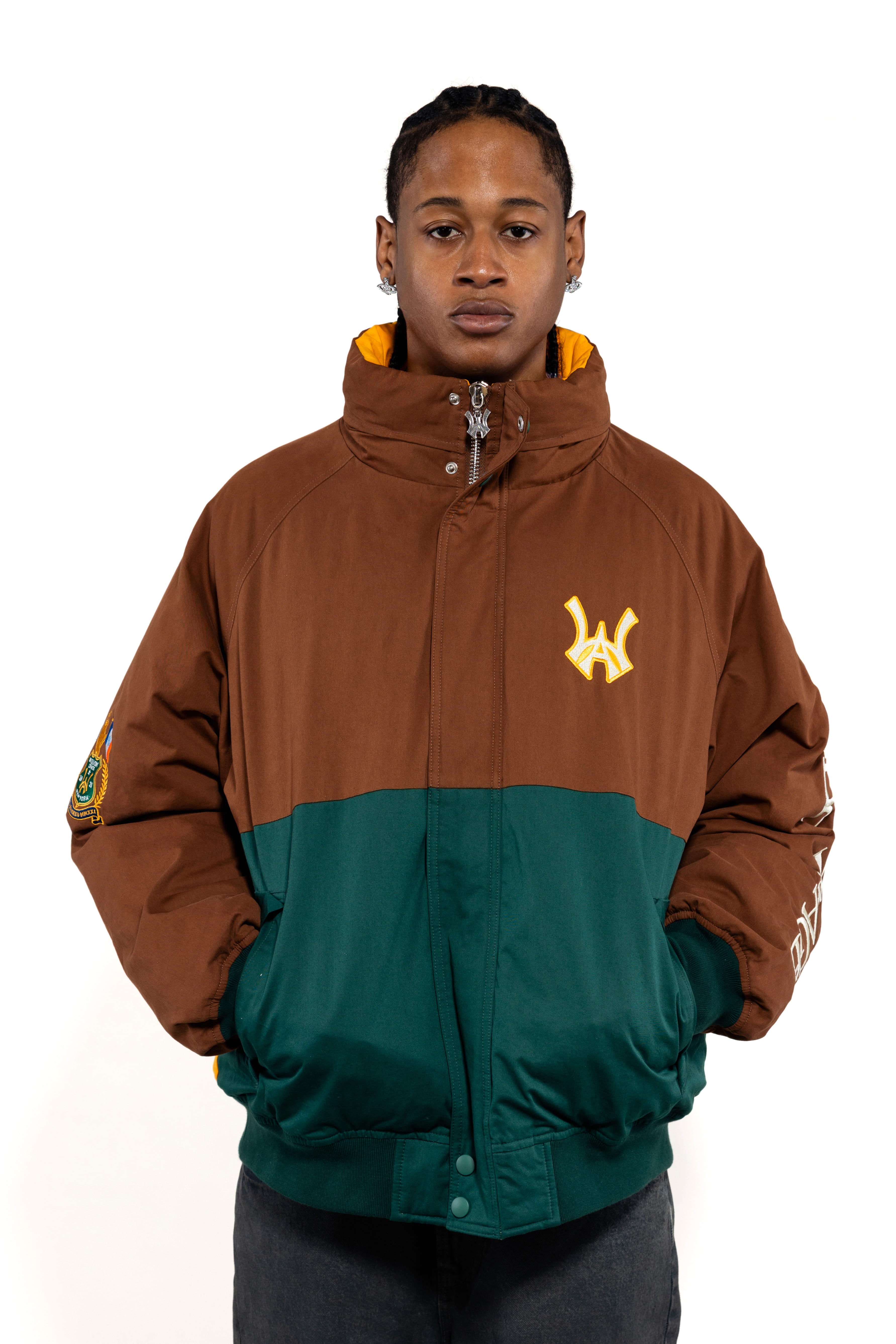 Close up view of a Male Model wearing a brown and forest green jacket with yellow accents on a white background. 'WA' Logo embroidered on the left 
