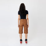 Rear view of a Female model wearing a black t-shirt and Wisdom of age canvas carpenter shorts in brick color on a light gray background