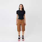 Female model wearing a black t-shirt and Wisdom of age canvas carpenter shorts in brick color on a light gray background