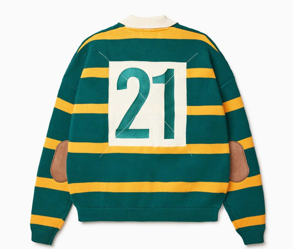 Rear View of the Wisdom of age Lemon rugby. This is a Green garment with yellow stripes, a cream collar. There is a embroidered number 21 within a cream box on the middle of the back and brown suede elbow patches on each sleeve.