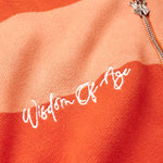 Close Up on the Front view of the WOA knit hoodie. Wisdom Of Age embodied on the right chest in between the alternating orange stripes. Chrome finish WA logo zipper visible on the top right.