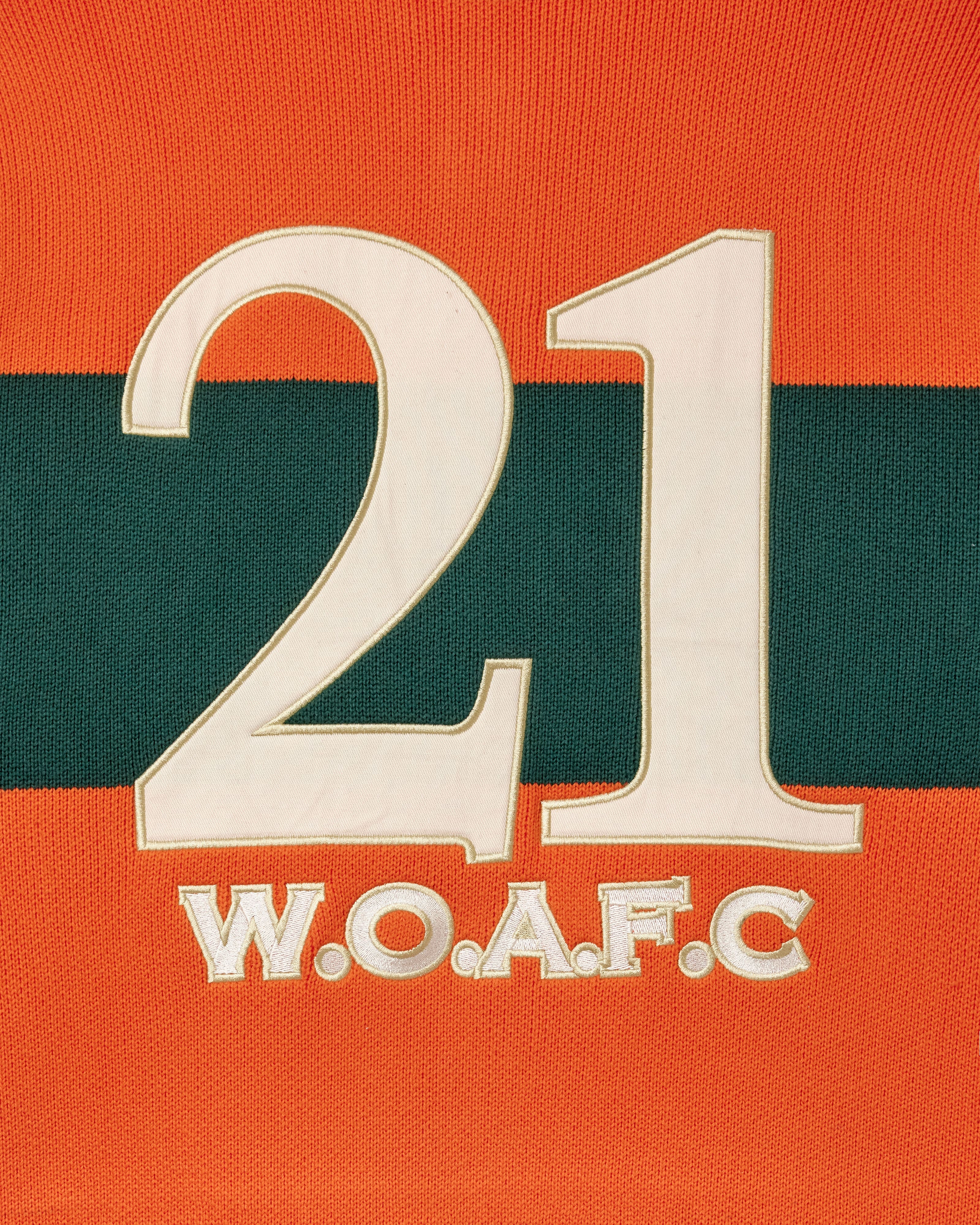 Close-up of the embroidery of the number 21 and 'W.O.A.F.C.' on an orange and green background