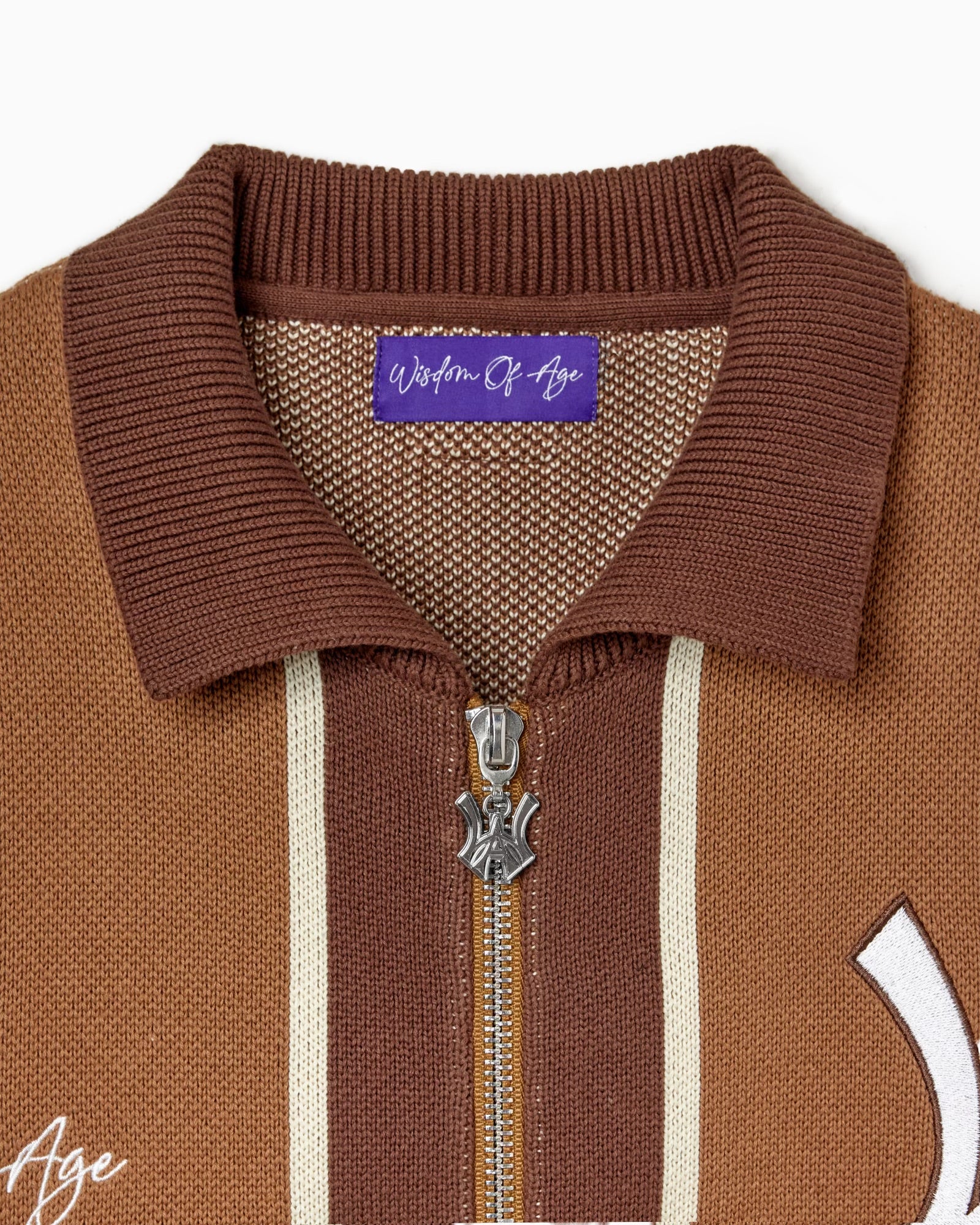 Close up view of the zipper and tag of the Wisdom Of Age Knitted Brown and beige striped cardigan on a white background.