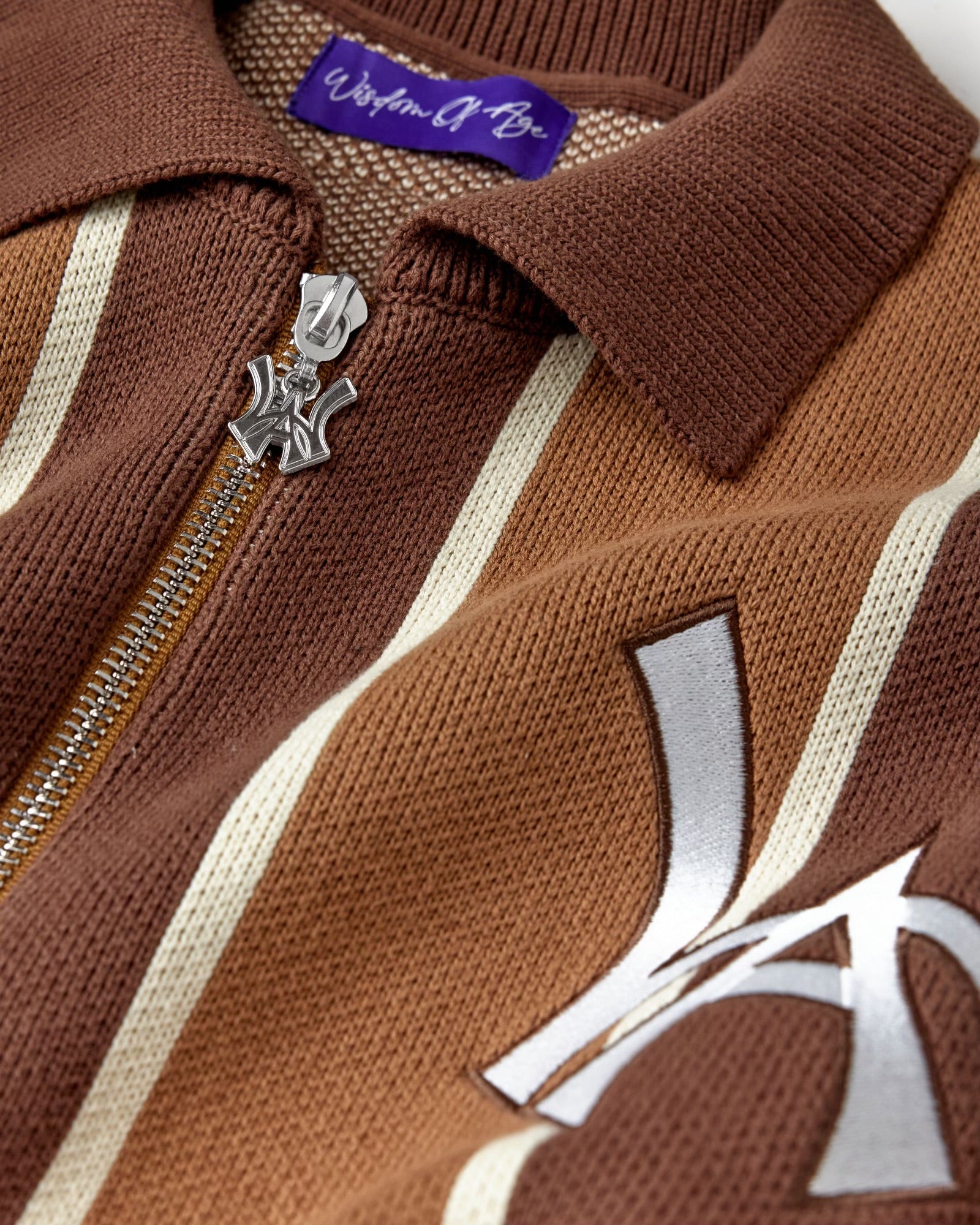 Close-up of the brown and beige patterned cardigan with a WA logo zipper and visible 'Wisdom Of Age' label.