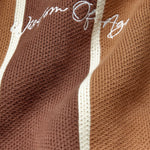 Brown knitted fabric with white 'Wisdom Of Age' embroidery on a brown background