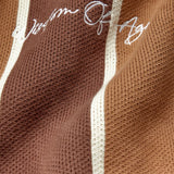 Brown knitted fabric with white 'Wisdom Of Age' embroidery on a brown background