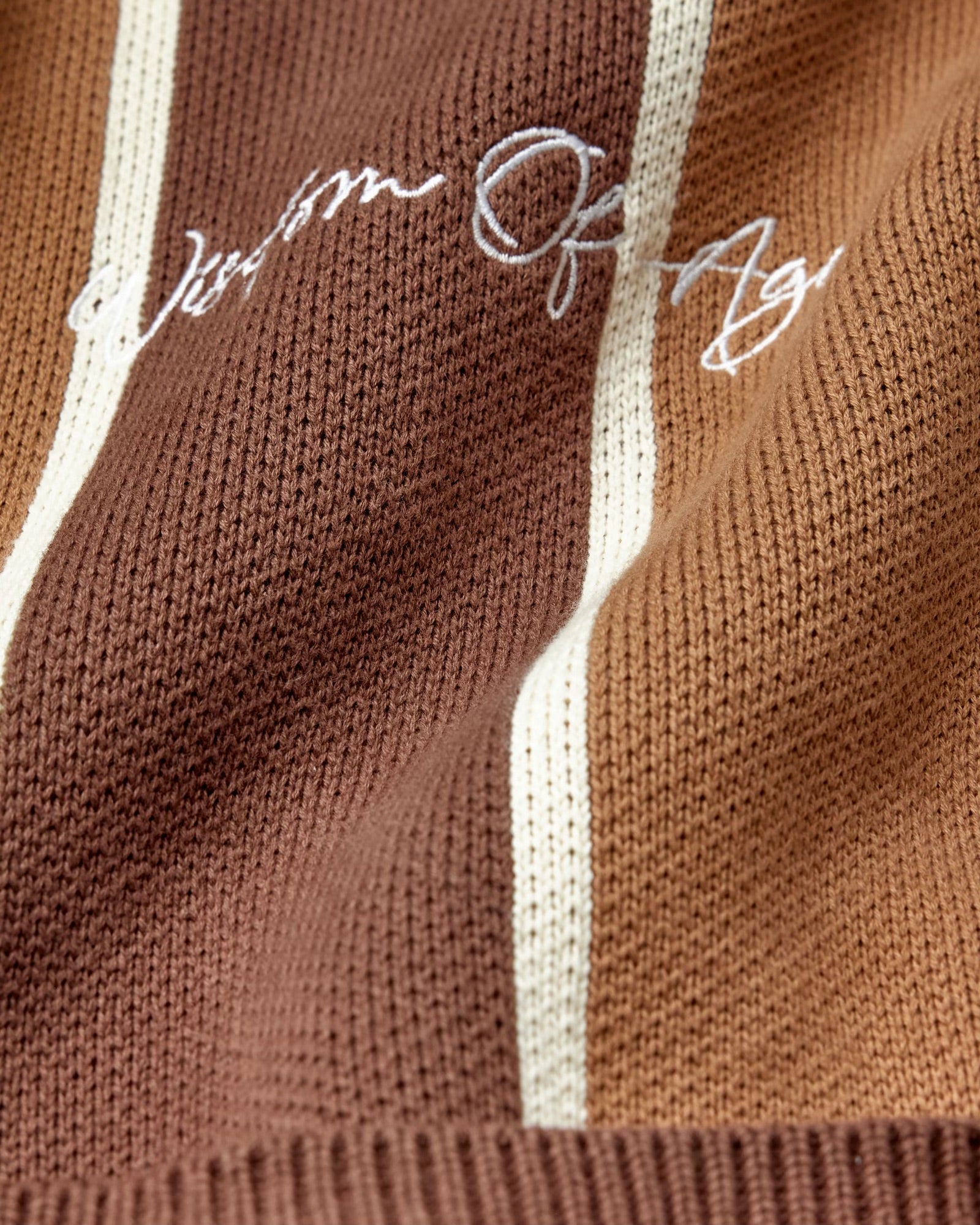 Brown knitted fabric with white 'Wisdom Of Age' embroidery on a brown background