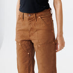 close up view of a Female model wearing a black t-shirt and Wisdom of age canvas carpenter shorts in brick color on a light gray background