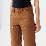 close up view of a Female model wearing a black t-shirt and Wisdom of age canvas carpenter shorts in brick color on a light gray background