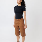 Side view of a Female model wearing a black t-shirt and Wisdom of age canvas carpenter shorts in brick color on a light gray background