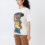 sideview of a Female model wearing a white t-shirt with cartoon characters and brown shorts on a light gray background