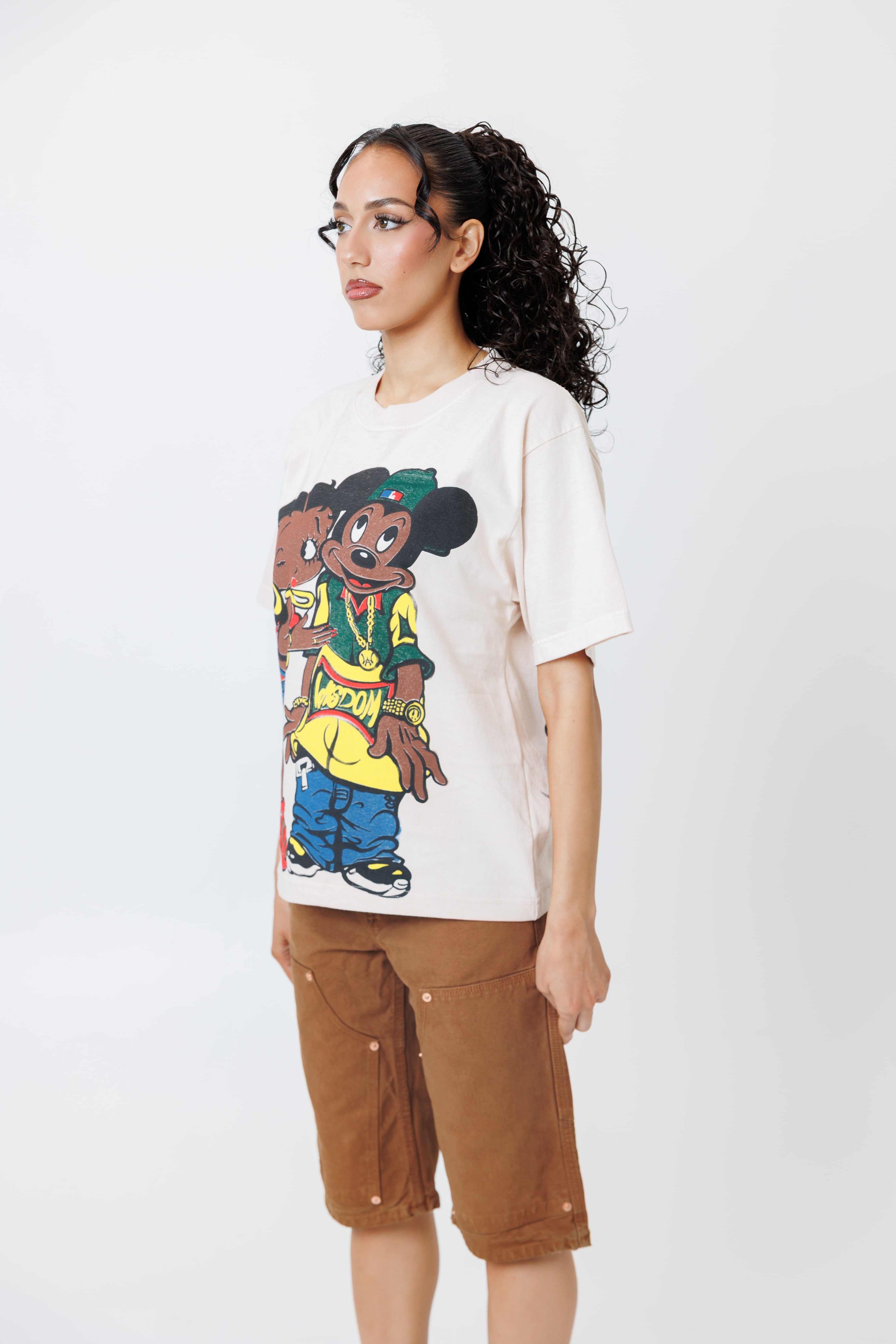 sideview of a Female model wearing a white t-shirt with cartoon characters and brown shorts on a light gray background