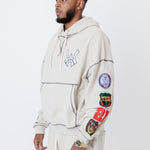 close up of a male model wearing a the W.O.A. Rugby Club Sweat suit in Sandstone with multiple embroidered patches on the sleeves and pant legs on a white background