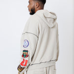rear view of a male model wearing a the W.O.A. Rugby Club Sweat suit in Sandstone with multiple embroidered patches on the sleeves and pant legs on a white background