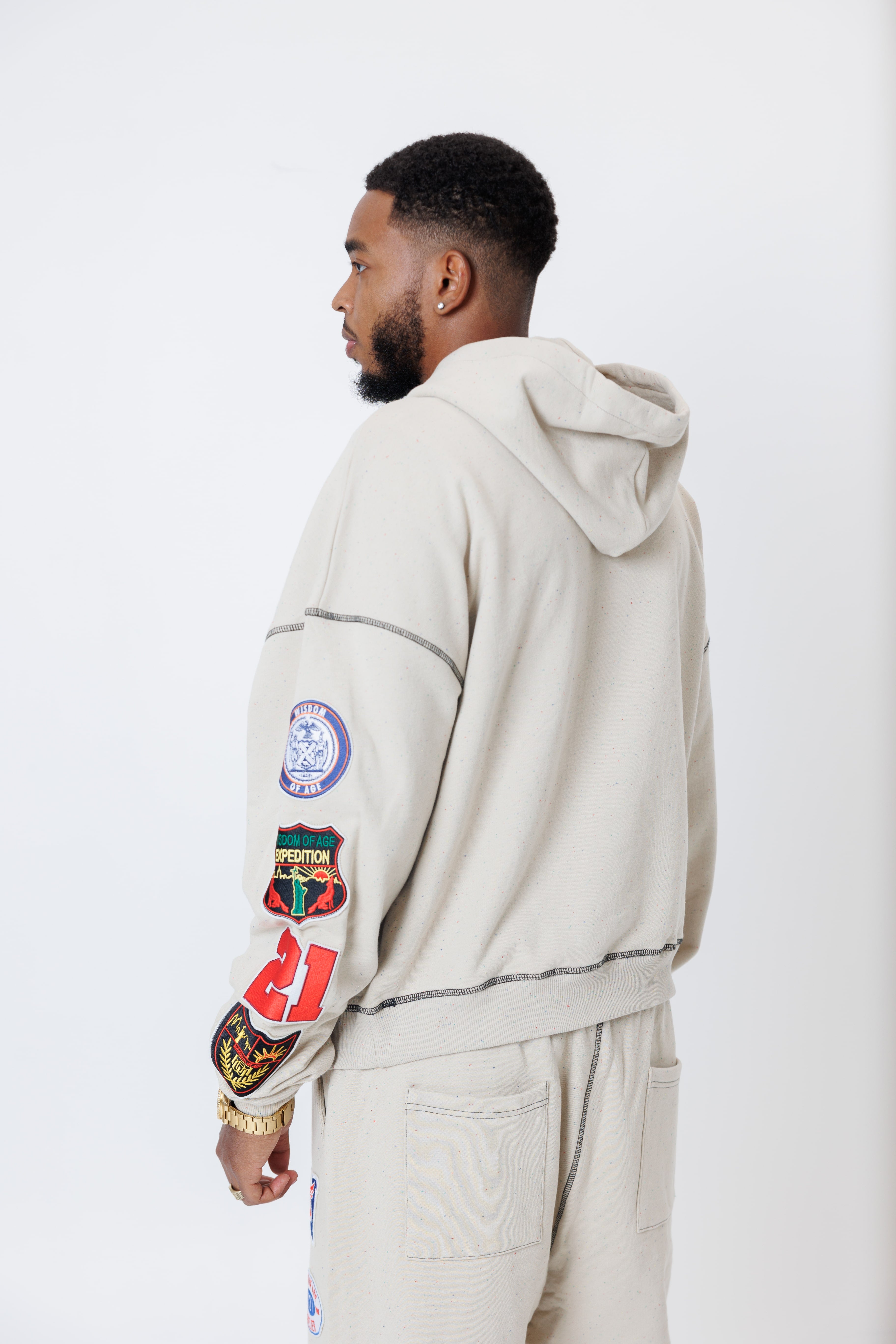 rear view of a male model wearing a the W.O.A. Rugby Club Sweat suit in Sandstone with multiple embroidered patches on the sleeves and pant legs on a white background