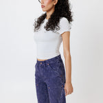 side view of a Female model wearing a white t-shirt and Wisdom of age canvas carpenter shorts in purple color on a light gray background