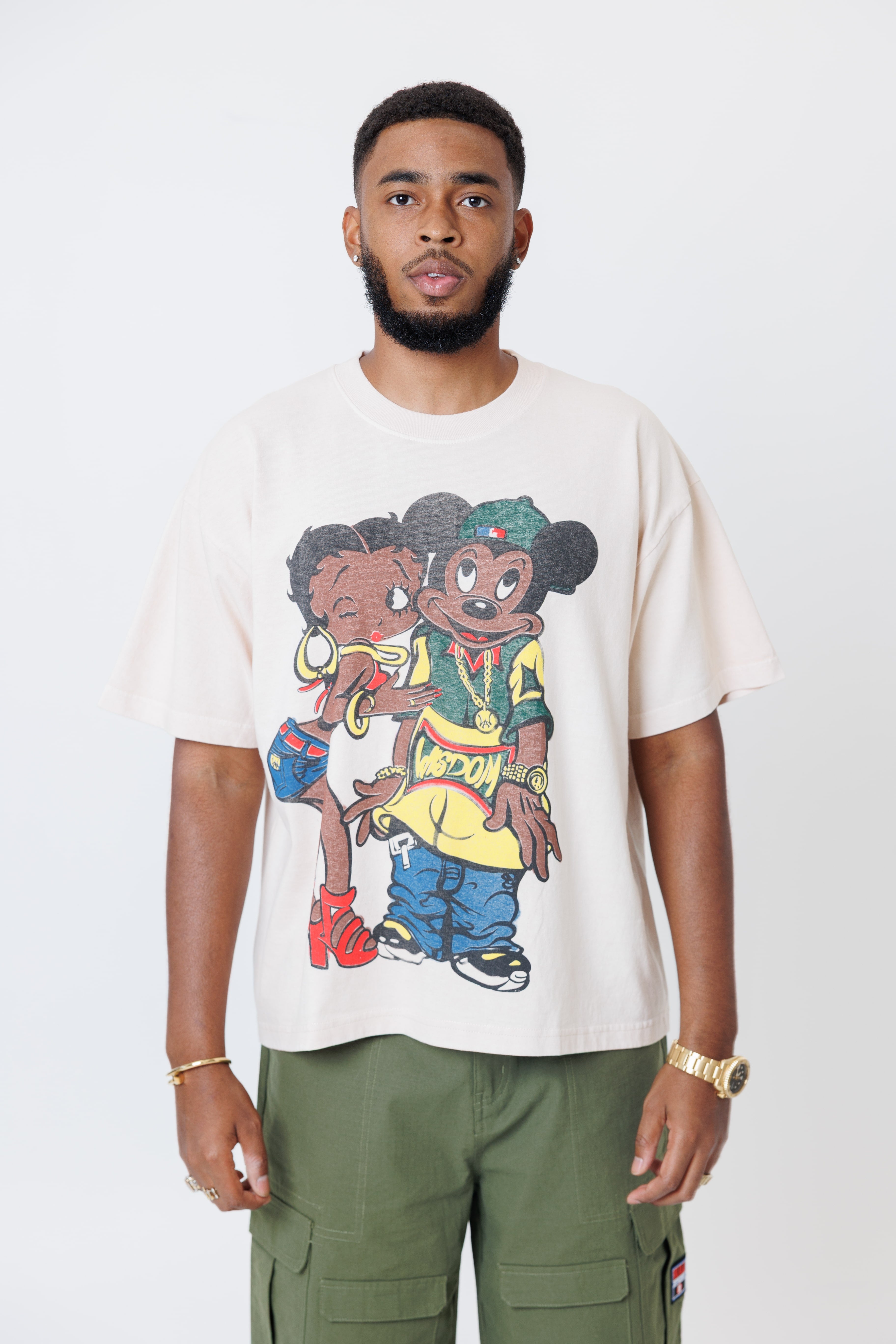 Male model wearing a off-white t-shirt with cartoon characters and olive cargo pants on a light gray background