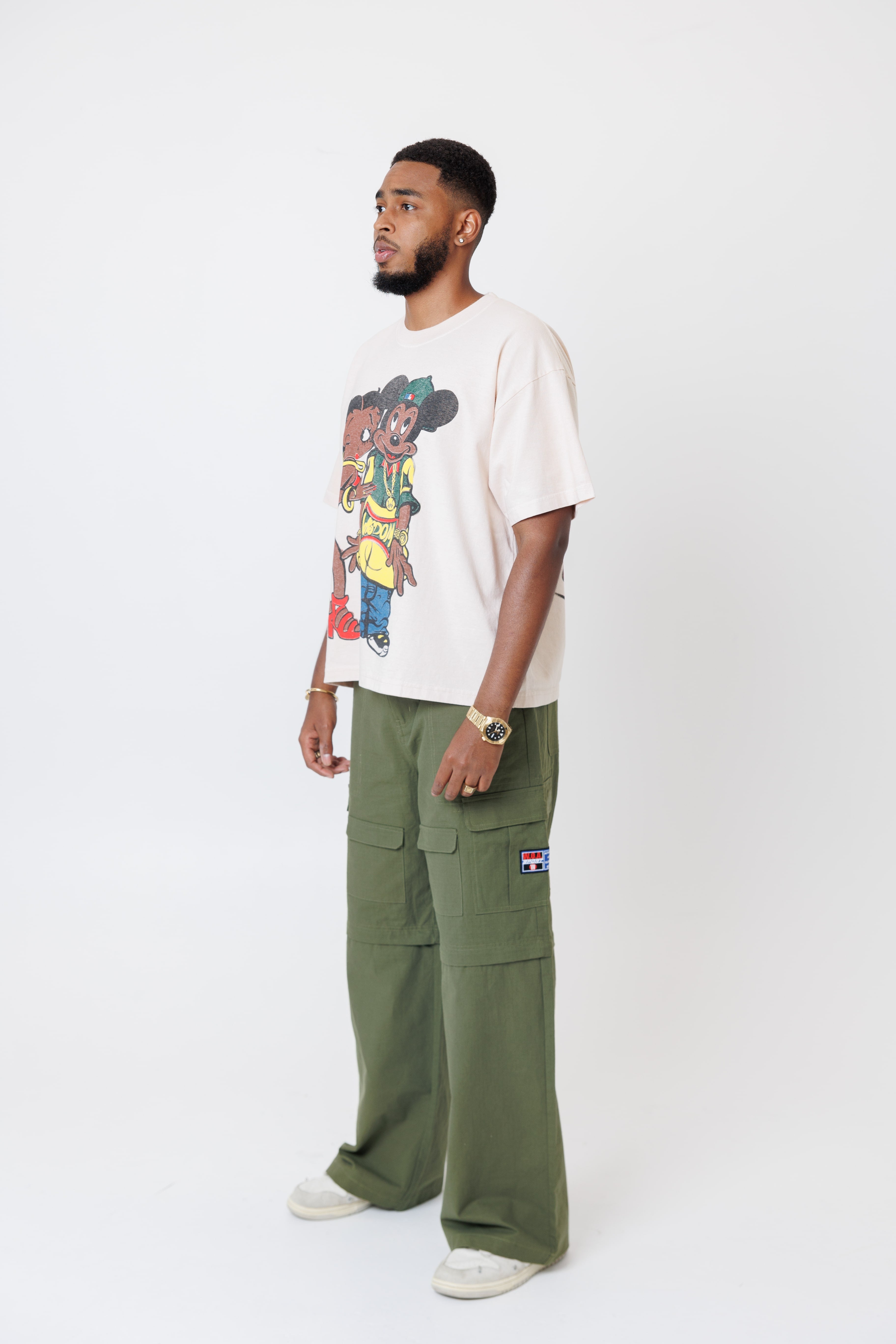 male model wearing a off-white t-shirt with cartoon characters and olive cargo pants on a light gray background
