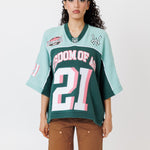 female Model wearing a the WOA Football jersey V2 in the Mint color with 'Wisdom Of Age' and number '21' embroidered on the front. Model is wearing the WOA canvas carpenter shorts on a white background.