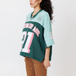side view of a female Model wearing a the WOA Football jersey V2 in the Mint color with 'Wisdom Of Age' and number '21' embroidered on the front. Model is wearing the WOA canvas carpenter shorts on a white background.