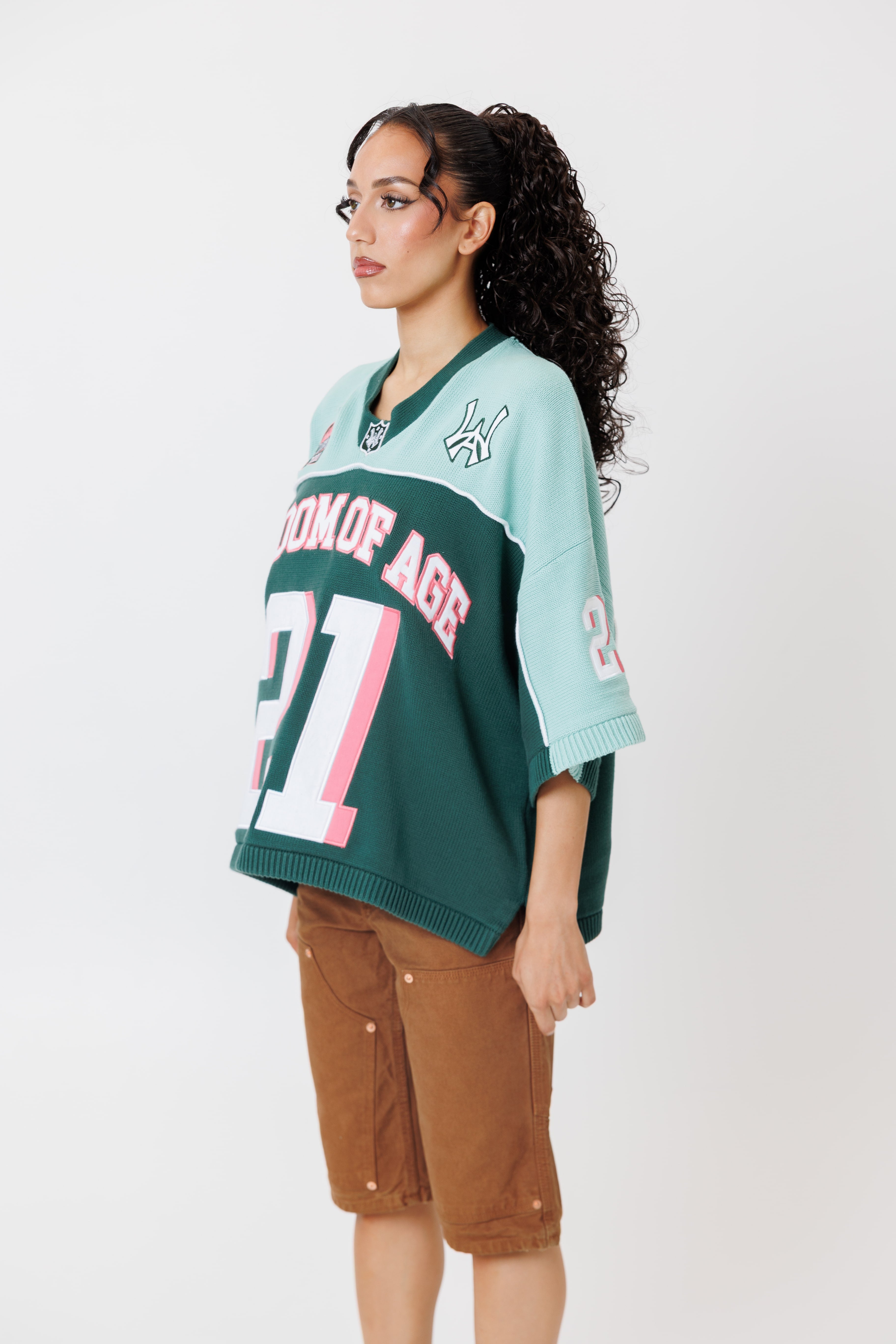 side view of a female Model wearing a the WOA Football jersey V2 in the Mint color with 'Wisdom Of Age' and number '21' embroidered on the front. Model is wearing the WOA canvas carpenter shorts on a white background.