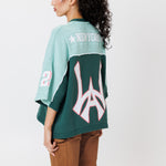 rear view of a female Model wearing a the WOA Football jersey V2 in the Mint color with 'Wisdom Of Age' and number '21' embroidered on the front. Model is wearing the WOA canvas carpenter shorts on a white background.