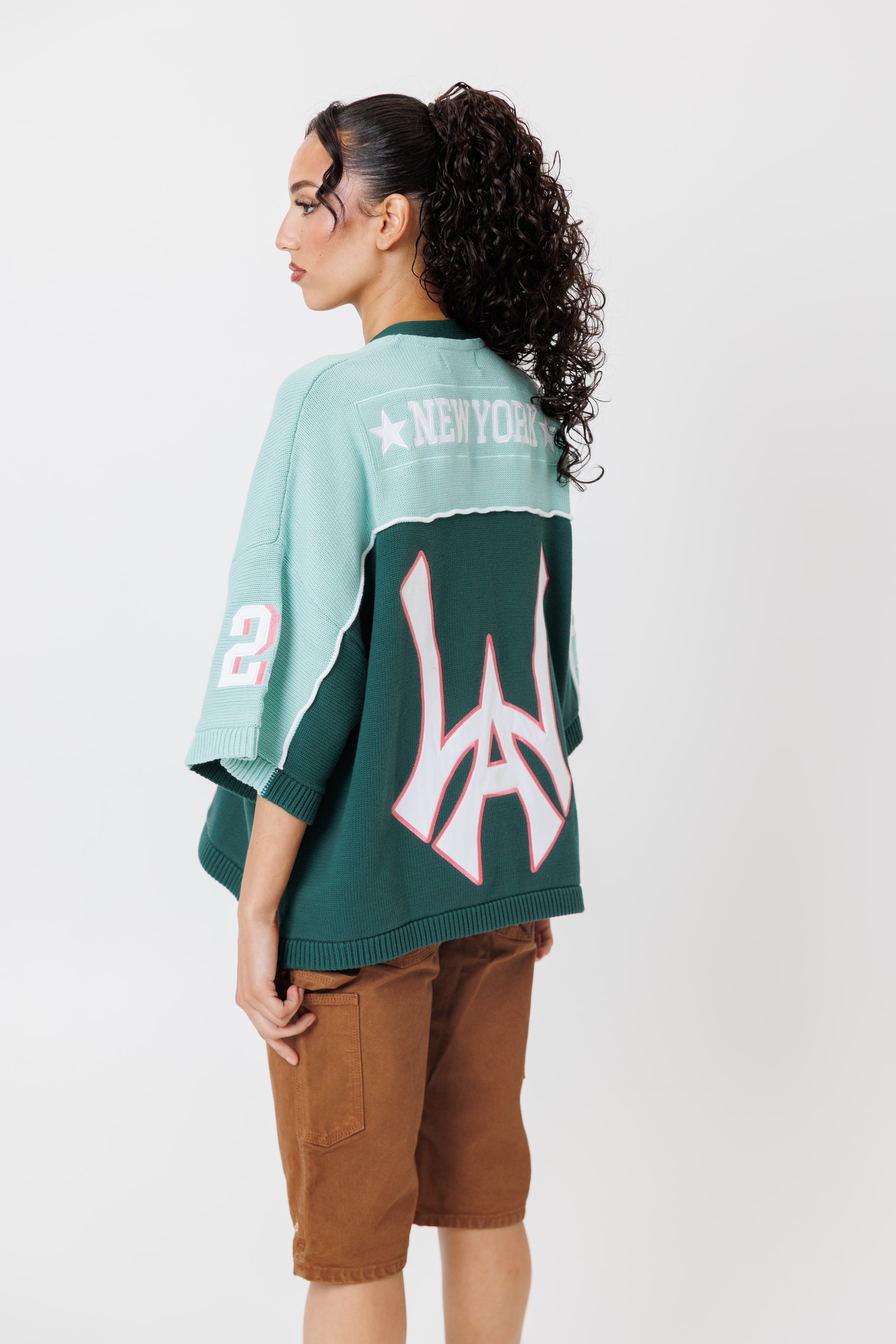 rear view of a female Model wearing a the WOA Football jersey V2 in the Mint color with 'Wisdom Of Age' and number '21' embroidered on the front. Model is wearing the WOA canvas carpenter shorts on a white background.