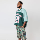 Side view of Male Model wearing a the WOA Football jersey V2 in the Mint color with 'Wisdom Of Age' and number '21' embroidered on the front. Model is wearing the WOA Camo Cargos on a white background.