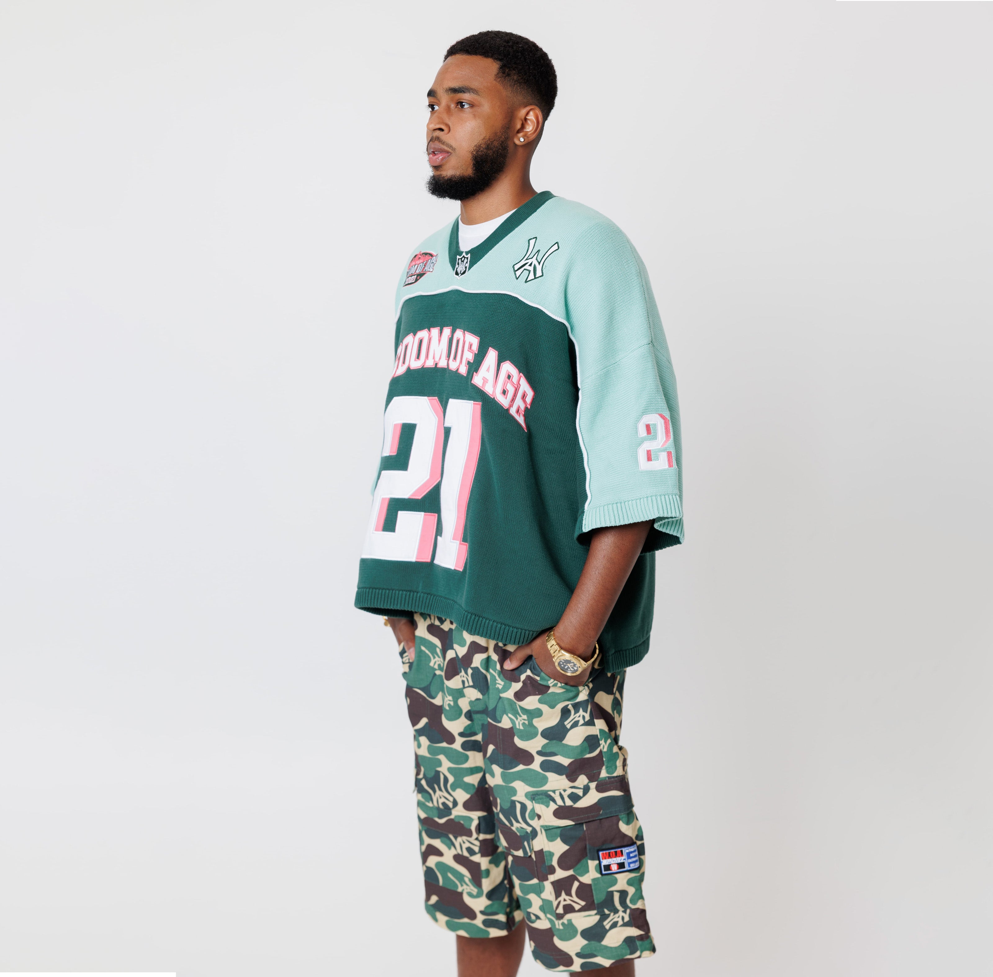 Side view of Male Model wearing a the WOA Football jersey V2 in the Mint color with 'Wisdom Of Age' and number '21' embroidered on the front. Model is wearing the WOA Camo Cargos on a white background.