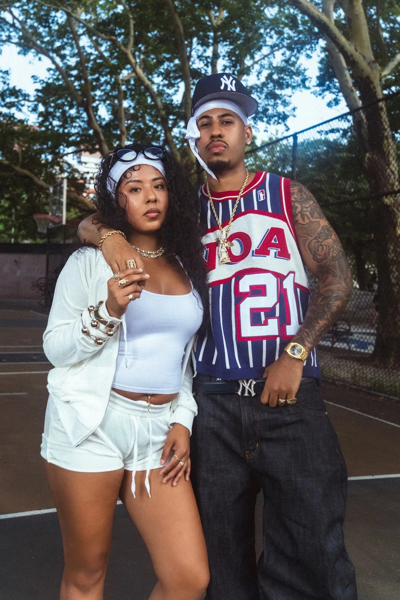 Female model in white clothing and male model wearing Wisdom Of Age Blue Pinstripe BasketBall jersey standing in outdoor basketball court.