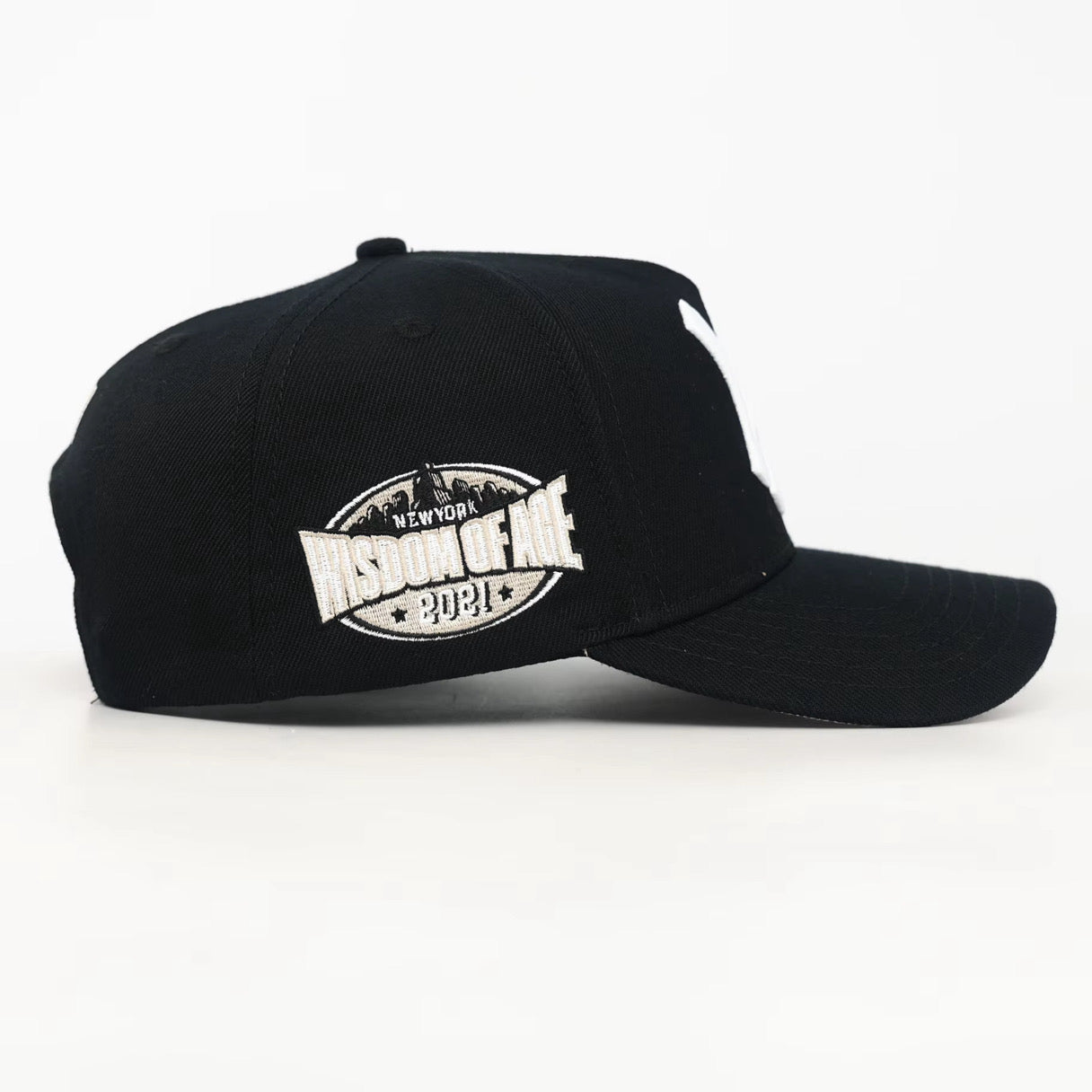 side view of a Black baseball cap with a white Wisdom of age logo on a white background