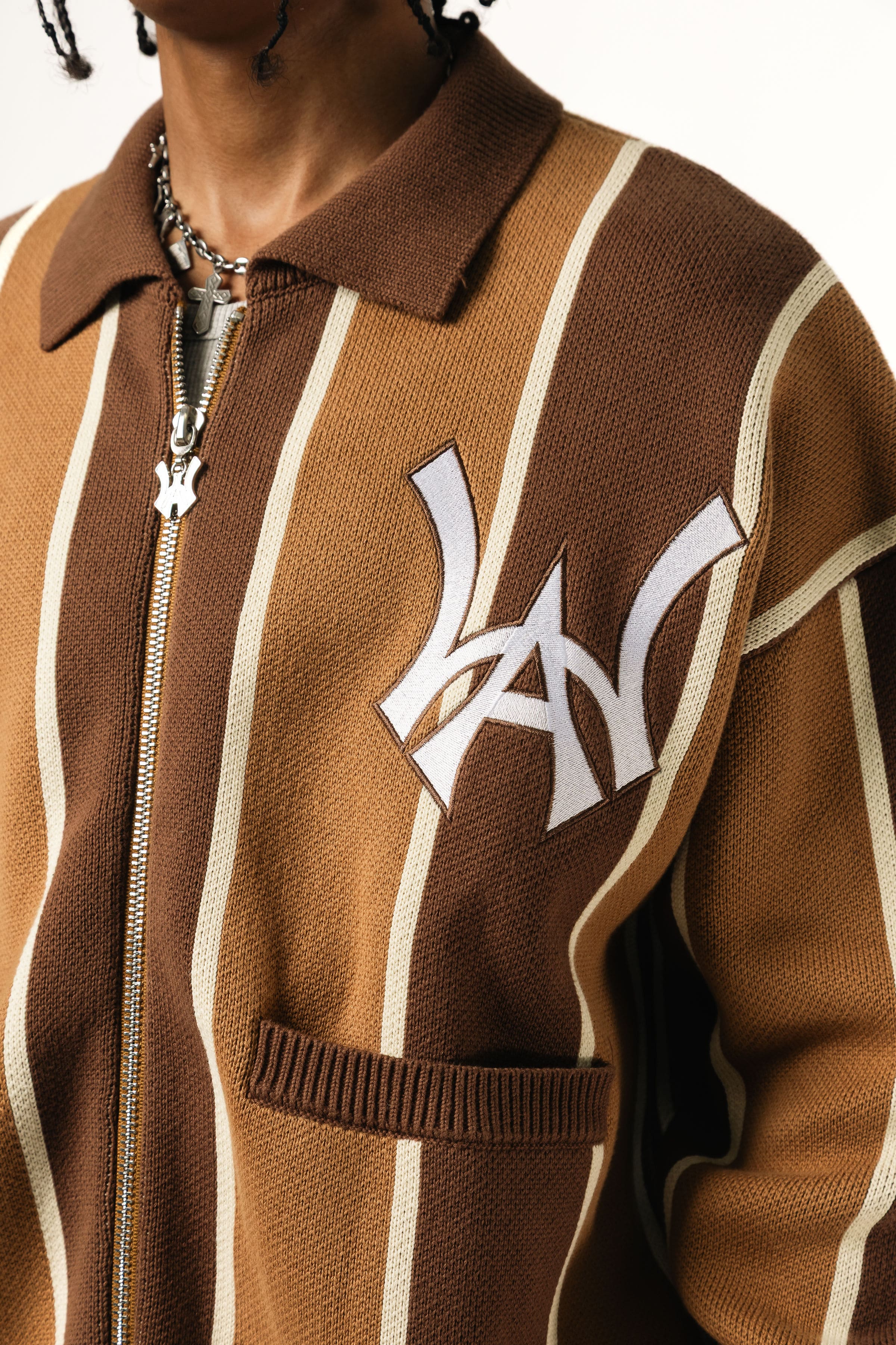 Close up of a Male model wearing the WOA Knitted Brown and beige striped cardigan with WA logo on the left chest and 'Wisdom Of Age' written in script on the right chest on a white background.