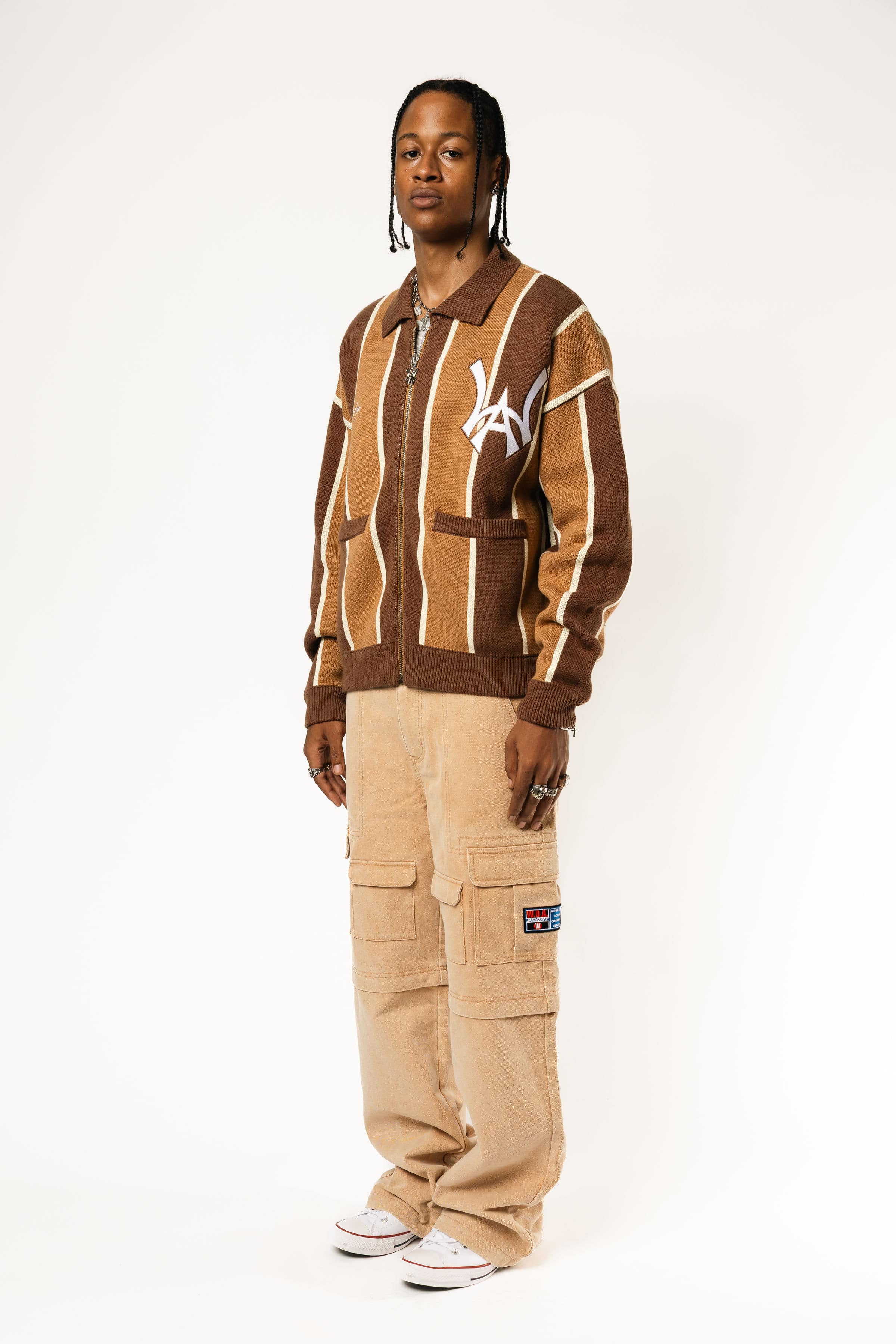 full body photo of a Male model wearing the WOA Knitted Brown and beige striped cardigan with WA logo on the left chest and 'Wisdom Of Age' written in script on the right chest on a white background.