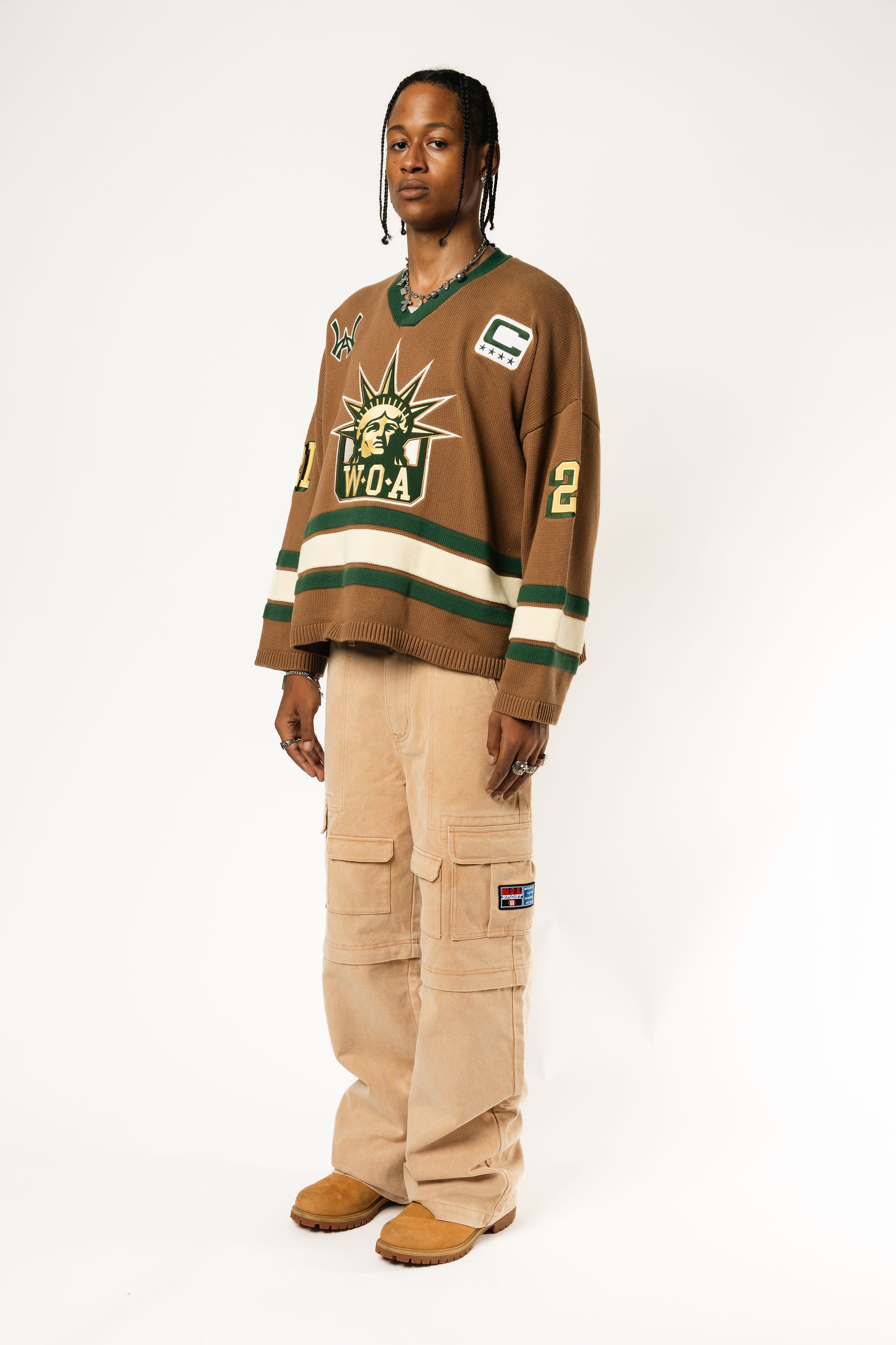 Full body photo of a Male Model wearing the WOA Knitted Hockey Jersey with Embroidered WA logo, Captains patch and W.O.A liberty graphic standing against a white background.