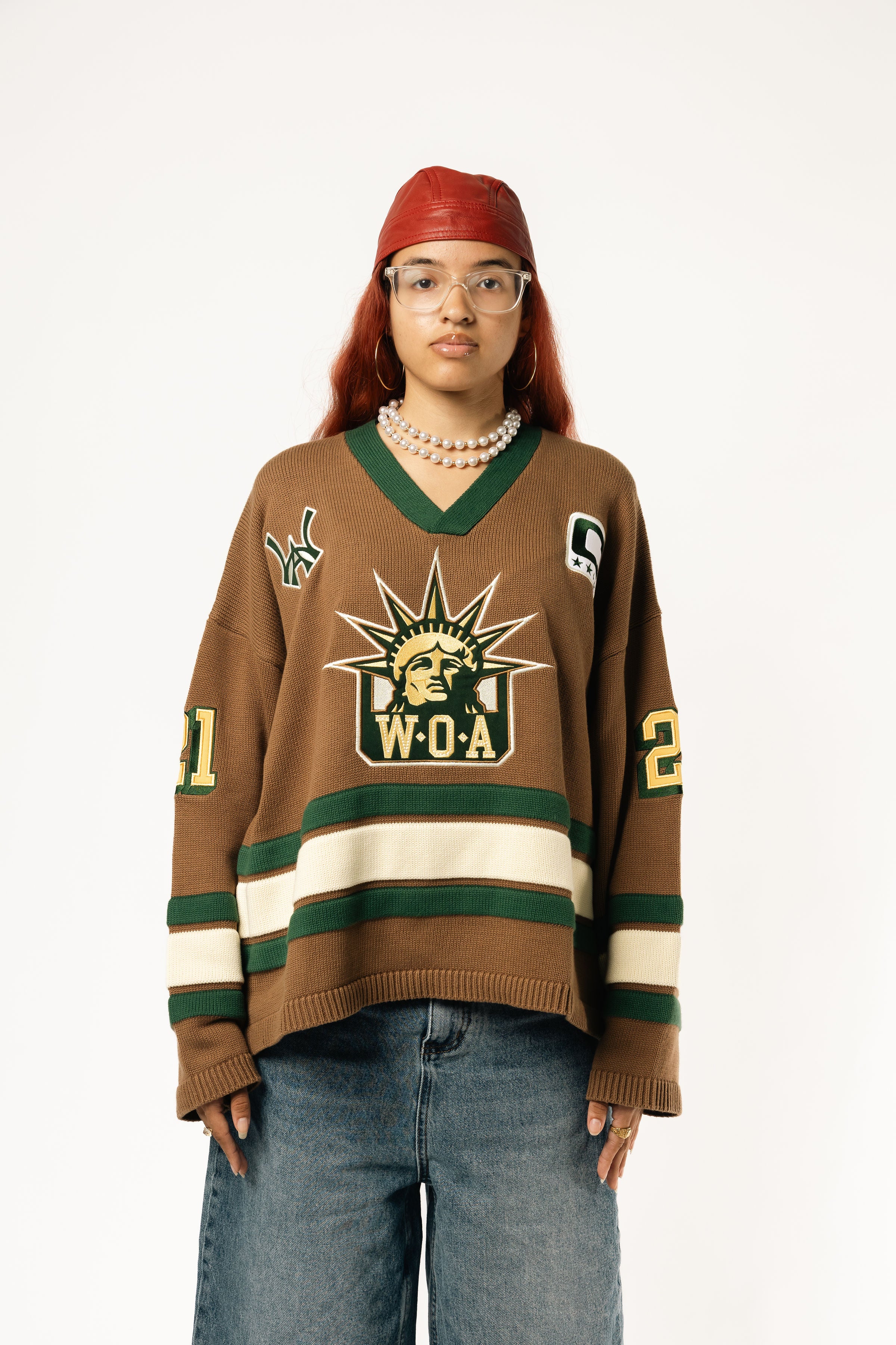 Female Model wearing the WOA Knitted Hockey Jersey with Embroidered WA logo, Captains patch and W.O.A liberty graphic standing against a white background.
