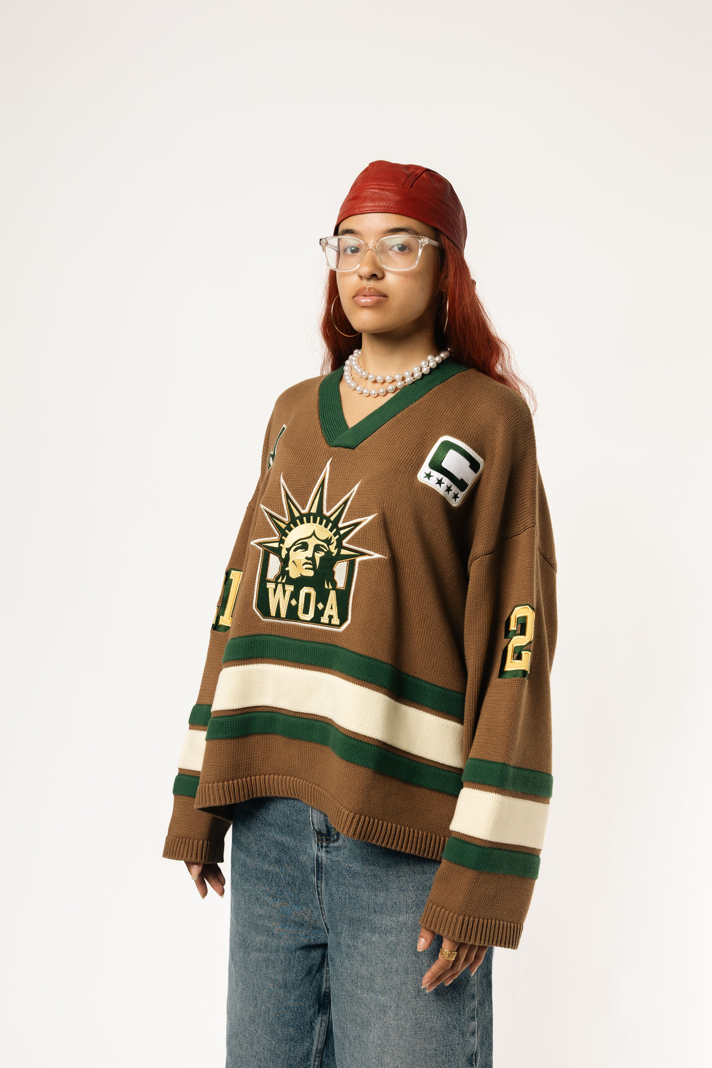 Front-side view of a Female Model wearing the WOA Knitted Hockey Jersey with Embroidered WA logo, Captains patch and W.O.A liberty graphic standing against a white background.