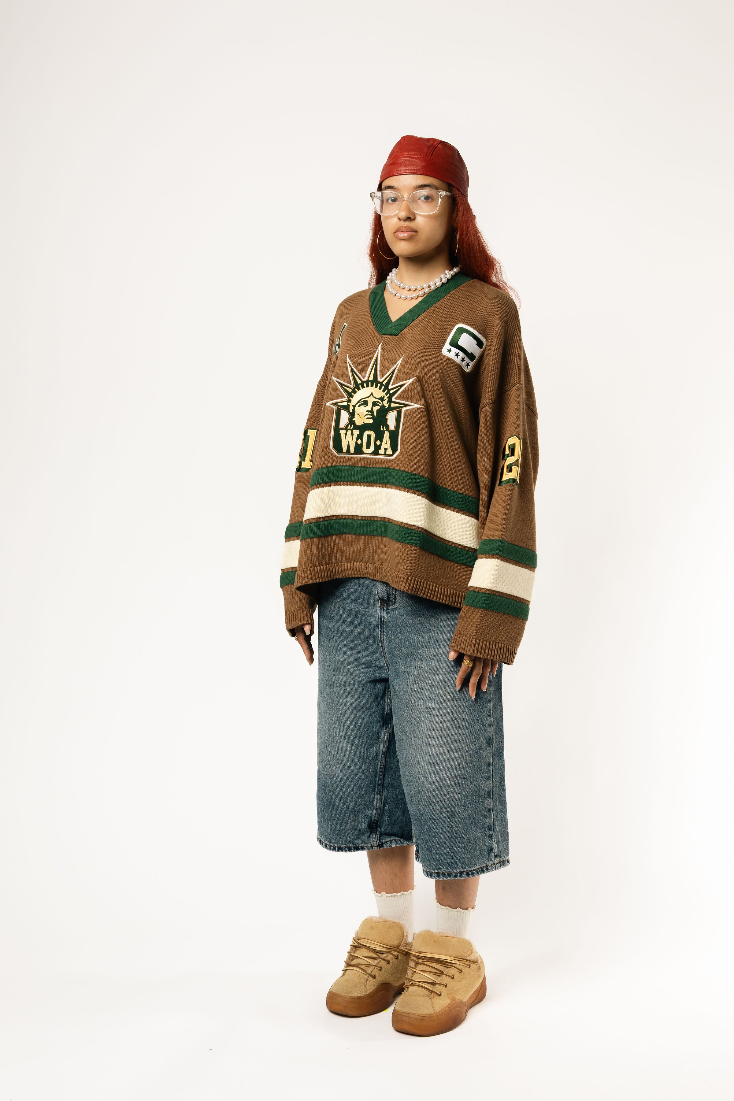 Full body view of a Female Model wearing the WOA Knitted Hockey Jersey with Embroidered WA logo, Captains patch and W.O.A liberty graphic standing against a white background.