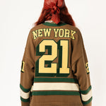 Rear view of a Female Model wearing the WOA Knitted Hockey Jersey with Embroidered 'NEW YORK' and the number 21 standing against a white background.