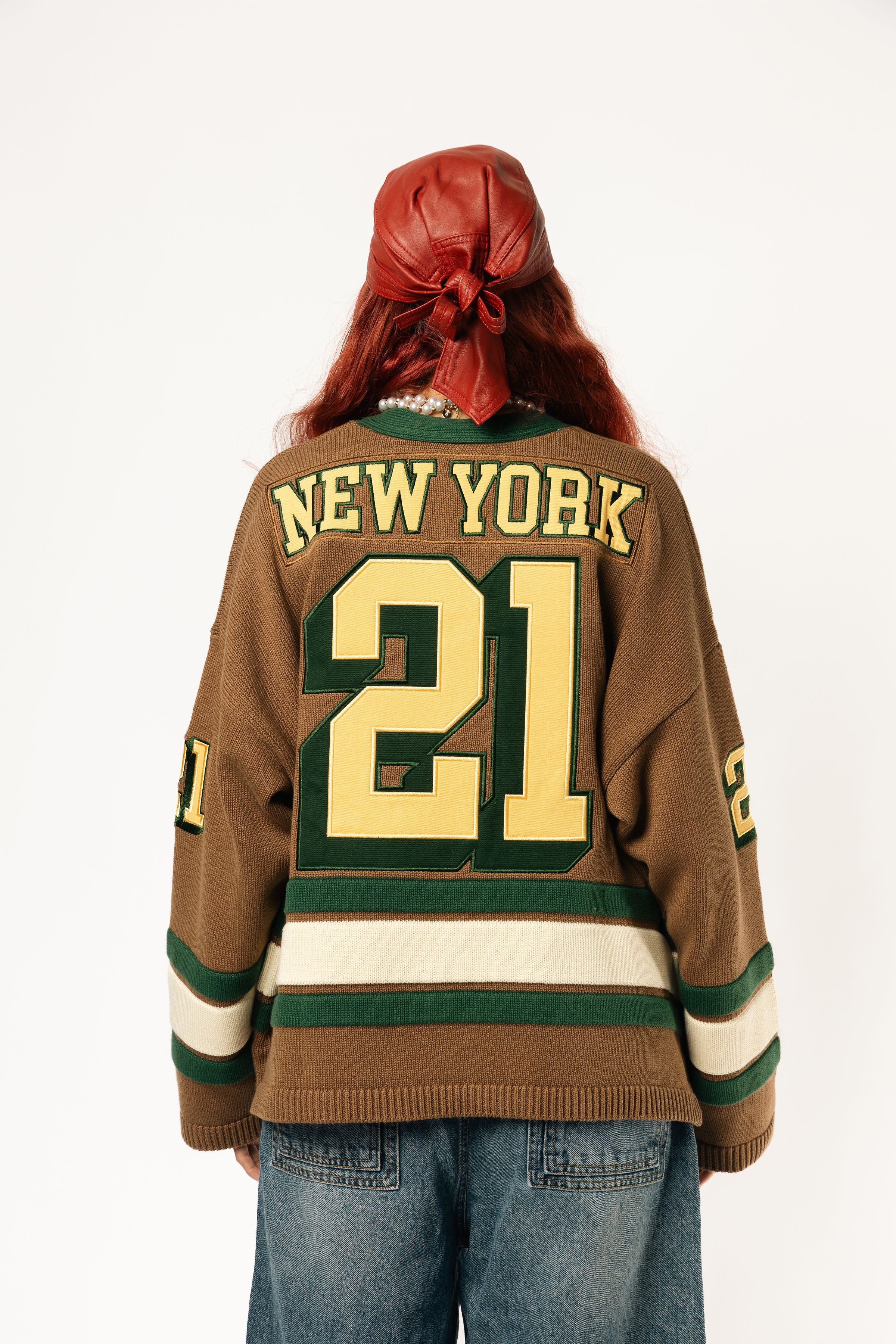 Rear view of a Female Model wearing the WOA Knitted Hockey Jersey with Embroidered 'NEW YORK' and the number 21 standing against a white background.