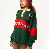 Side-front view of a Female Model wearing a green and red, knitted rugby sweater with 'Wisdom of Age' text on a white background.